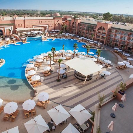 Savoy Le Grand Hotel Marrakech Marrakesh Bagian luar foto The photo shows a large, luxurious hotel resort with a spacious swimming pool at its center. The pool area features several lounge chairs and umbrellas arranged around the water, providing a relaxing atmosphere for guests. Surrounding the pool are la